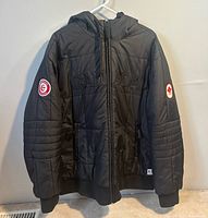 Front view of black quilted hooded Team Canada jacket on hanger
