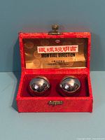 Open red brocade box showing two polished iron Baoding balls and interior label