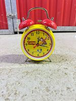 Front view of yellow Curious George twin-bell alarm clock on floor