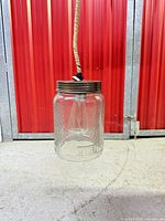 Full view of hanging mason jar light showing rope cord, metal lid and clear jar