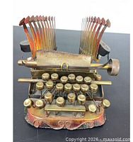 Front view of brass-plated metal typewriter sculpture showing keys and hammer arms