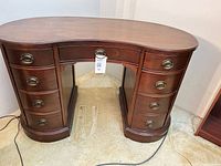 Front view of rosewood kidney-shaped desk showing eight drawers and brass pulls