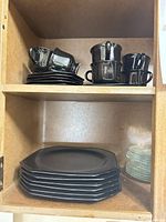 Black cups, saucers and plates on upper shelf