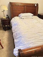 Queen sleigh bed headboard, footboard, round side table and lamp visible