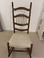 Front view of oak rocking chair showing spindle back and upholstered seat