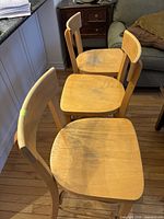 Three blonde wooden bar stools aligned, showing seats and backs