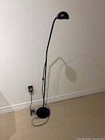 Full view of black floor lamp showing adjustable neck, dome shade, round base, power cord