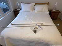 two silver curtain rods and bag of brass rings displayed on bed