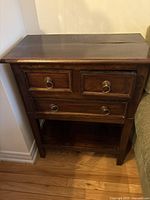 Front view of dark stained teak table showing drawers and shelf