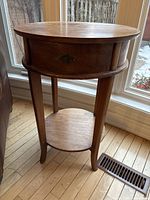 Front view of round teak side table showing drawer, legs, lower shelf