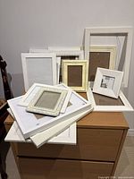 Overall lot of stacked white and cream photo frames on dresser