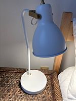 Side view of lamp on wicker nightstand showing base, angled stem, brass joint, and shade