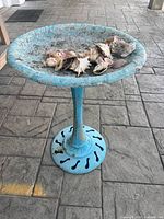 Full view of blue cast-iron birdbath with shells, showing pedestal and base