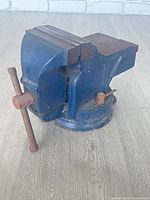 Side view of blue bench vise showing jaws, screw handle and swivel base