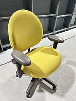 Front three-quarter view of yellow rolling office chair showing armrests, seat, backrest and base