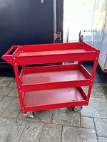 Full view of red three-shelf rolling cart showing shelves, handle and casters