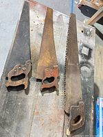 Three hand saws laid out on workbench showing overall size differences