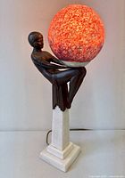 Lamp lit showing orange mottled globe shade and figure on marble pedestal