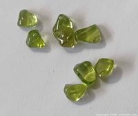 Eight polished peridot stones on white background, varied shapes