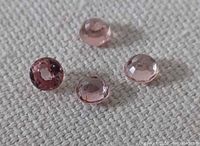 Four round faceted pink champagne zircons on textured surface