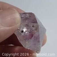 Raw amethyst point held between fingers showing facets and inclusions