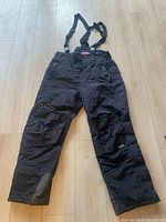 Full view of black HJC snow pants with suspenders laid flat