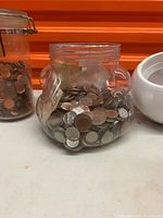Tall clamp-top jar with pennies beside bulbous jar with mixed coins