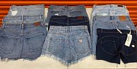 Overview of eight denim shorts laid out three columns; visible brand patches and Guess logo