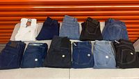 All eleven folded jeans laid out showing color variety and logo patches