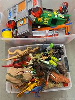 Two clear totes filled with dinosaur figures, vehicles and playset parts