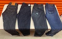 Four pairs jeans laid flat on table: dark Levi's, dark Guess, grey, blue