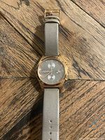 Full view of watch showing rose gold case and grey leather strap