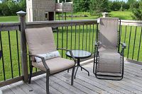 Wide shot of two patio chairs and small metal round table on wooden deck, green lawn in background