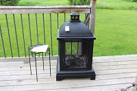 Firepit and small metal table shown on a wooden deck railing outside with field background