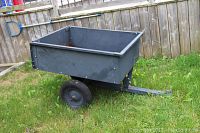 Side view of small metal trailer wagon standing on grass, showing overall construction and wheels.