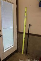 Photo showing the 6-foot yellow level and 49-inch black crow bar leaning against a wall near a door.