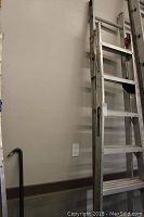 Full view of the aluminum extension ladder leaning against a wall, showing height and overall condition including rust patches.