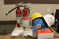 Full lot overview showing hard hats, fire extinguishers, gloves, goggles, and pencils arranged on a wooden surface.