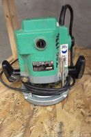 Front view of green and silver Hitachi router with black handles and power cord wrapped around base.