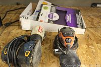 Top view of both electric sanders with cords coiled and partial sandpaper packs in box behind them.