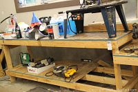Full view of the large wooden work bench with items placed on top (items not included). The bench has a natural wood frame and a particle board top with an extension attached on the side for a vice.