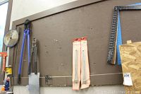 Wide shot of two large cutters with blue handles, squares, and saw hanging on brown wall