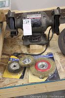 Full view of the bench grinder with two grinding wheels and three wire wheel brushes in original packaging on a wooden surface.