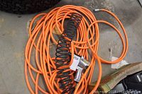 Photo showing the orange air hose coiled with the black coiled cord and air impact wrench on top.