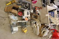 Wide view of laundry sink, boxes of plumbing supplies, metal brackets, clamps, and hoses on concrete floor.