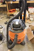 Front view of orange Ridgid shop vac with hose connected and power cord wrapped at top