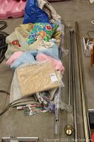 Photo showing assortment of curtain rods, various curtain fabrics, and two throw pillows on floor including a brightly colored floral pillow.
