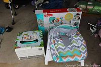 Fisher Price portable rocker and Bumbo Multi-Seat in original boxes, rocker seat unfolded showing colorful chevron pattern.