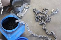 Tow chain partially coiled outside and inside blue plastic container, showing heavy gauge metal links.