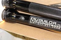 Photo showing close-up of two large black flashlights, one branded U-Buildr Ltd with contact info.